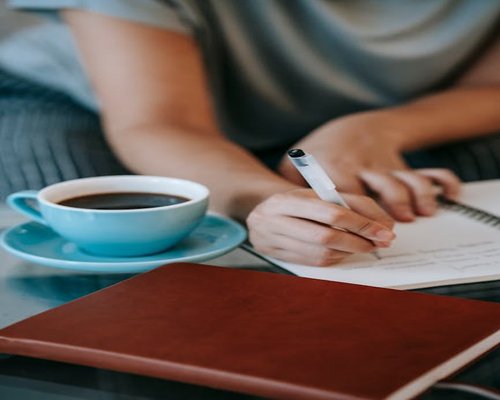 Woman writing a checklist in a notebook while drinking coffee